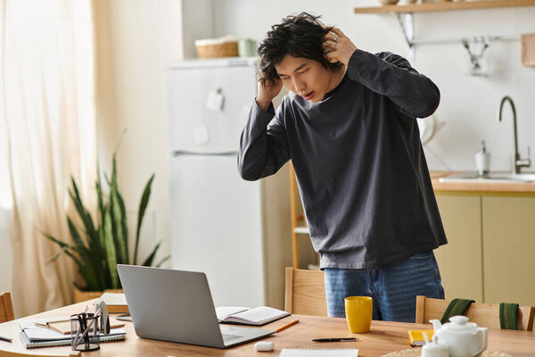 A young Asian student struggles with his online studies at home, feeling overwhelmed and stressed.