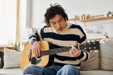 Yakışıklı bir Asyalı genç adam akustik gitarını evde çalmayı öğrenmeye odaklanıyor..