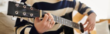 Genç bir adam, rahat bir odada akustik gitar çalıyor.