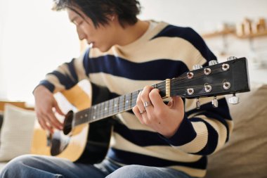 Genç bir adam akustik gitar yeteneklerini özenle, sıcak ve davetkar bir yerde çalışır..