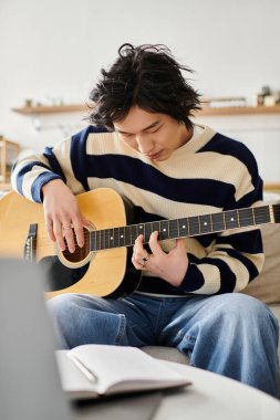Genç bir adam akustik gitarda rahat bir ortamda ustalaşmaya odaklanmış..