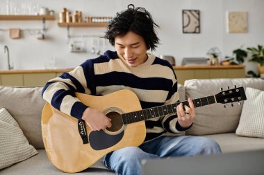 Huzurlu bir oturma odasında, genç Asyalı bir adam akustik gitar çalmayı zevkle öğrenir..