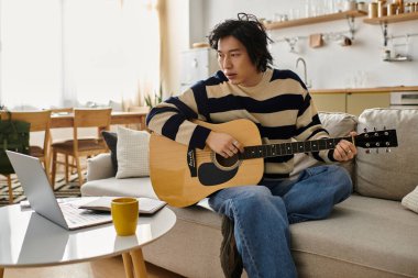 Yakışıklı genç adam evde rahat otururken akustik gitar öğrenmeye odaklanıyor..