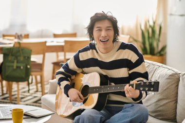 Yakışıklı Asyalı genç adam sıcak, davetkar bir atmosferde evde akustik gitar öğrenmekten hoşlanıyor..