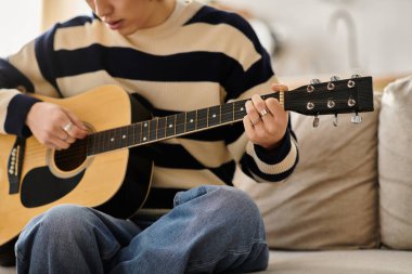 Genç bir adam rahat evinde akustik gitar tıngırdatarak pratik yapıyor..