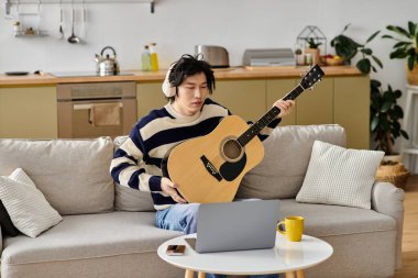 Genç Asyalı bir adam akustik gitarını evde çalmayı öğrenirken dikkatle odaklanır..