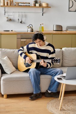 Yakışıklı genç adam rahat bir evde akustik gitar çalmayı öğrenmekten hoşlanıyor..
