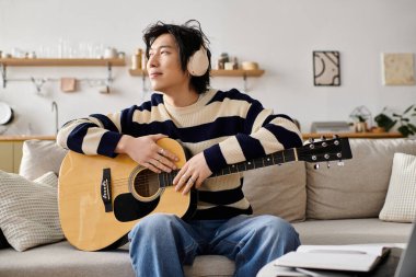 Handsome young man learns guitar while enjoying a comfortable afternoon at home. clipart