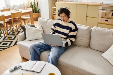 Yakışıklı Asyalı genç adam rahat bir koltukta otururken internetten öğrenmeye daldı..