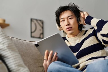 Odaklanmış genç bir adam evinde rahatça otururken tabletini kullanarak internetten ders çalışıyor..