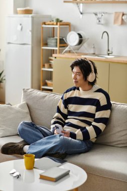 Genç adam şık bir oturma odasında, kulaklıkla müzik dinliyor.