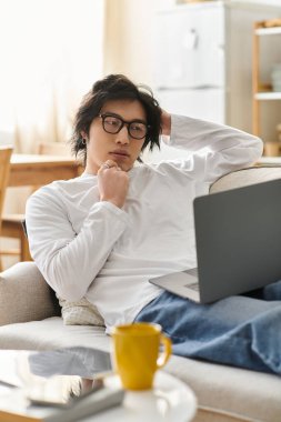 Genç bir adam kanepede rahat bir şekilde oturur, dizüstü bilgisayarıyla online çalışmalar yapar..