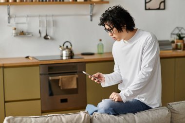 Şık bir genç adam koltuğunda rahatlar, rahat bir evde akıllı telefonunu dikkatle karıştırır..