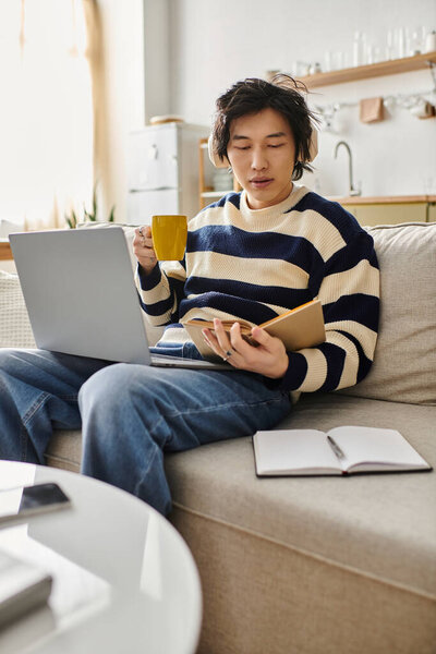 Красивый молодой человек удобно сидит дома и занимается онлайн-обучением, потягивая свой напиток..