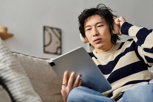 A focused young man studies online using his tablet while sitting comfortably at home.