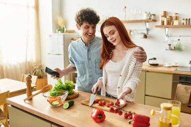 Genç bir çift, parlak ev mutfağında yemek pişirip, lezzet ve neşeyi harmanlayarak kaliteli zaman geçirmeyi sever..