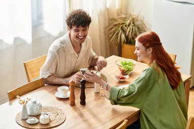 Genç çift rahat evlerinde gülücüklerini ve kahkahalarını paylaşırken hafif bir yemeğin tadını çıkarıyor..