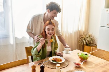 Neşeli genç bir çift evde yemek yerken kahkaha ve sevgiyi paylaşıyor, sevgi dolu anlar yaratıyorlar..