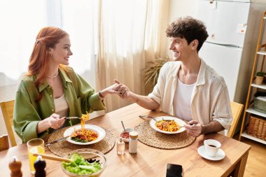 Sıcak bir mutfakta, bir çift güzel bir yemeği paylaşıyor, gülüyor ve makarna yerken kaynaşıyor..