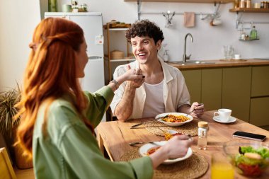 Şık bir mutfakta, genç bir çift yemek yiyor, neşeyi ve yiyecekle bağlantıyı paylaşıyor..