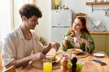 Genç bir çift evde keyifli bir yemek yer, birbirlerine eşlik eder ve gülerler..