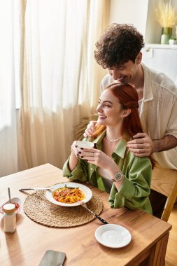 Genç bir çift evde keyifli bir yemek yiyor, gülüyor ve birbirlerine bağlanıyorlar..