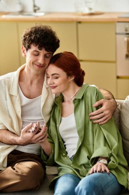 Genç bir çift rahat bir kanepede birlikte vakit geçirmenin keyfini çıkarıyor. Evlerinde gülümseme ve sıcaklığı paylaşıyorlar..