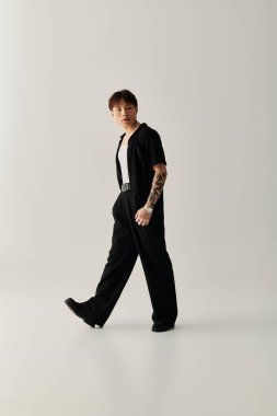 Siyah kıyafetli genç adam sanatsal bir mekanda cesur ve şık bir görünüm sergiliyor..