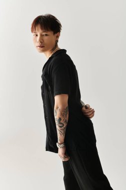 Şık Asyalı genç adam kendine güvenerek poz veriyor, gösterişli bir ortamda dövmelerini gösteriyor..