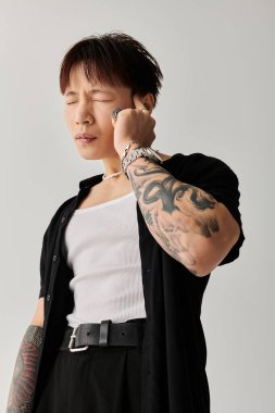 Genç yakışıklı bir adam minimalist bir stüdyoda duruyor, eşsiz stilini ve dövmelerini sergiliyor..