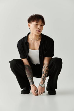 Genç, modaya uygun Asyalı bir adam kendine güven ve cazibe yayarak çömelip tarzını sergiliyor..