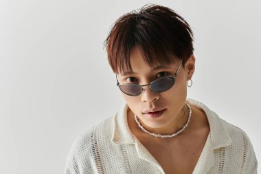 Şık, genç bir Asyalı kendine güvenerek poz veriyor, son moda güneş gözlüklerini ve kıyafetlerini vurguluyor..