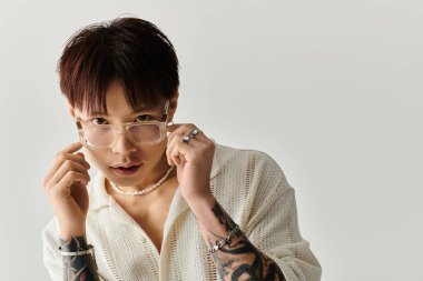 Genç yakışıklı bir Asyalı gözlüğünü ayarlıyor, şık bir görünüş ve karmaşık dövmeler sergiliyor..