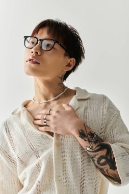 Gözlüklü, dövmeli, modaya uygun genç Asyalı bir adam kendine güvenini ve tarzını sergiliyor..