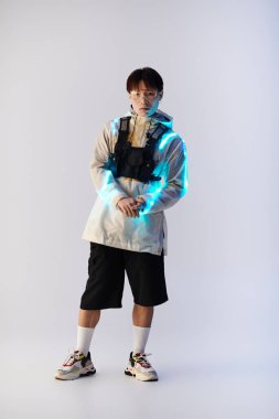 Yakışıklı Asyalı genç bir adam kendine güvenerek ayakta duruyor. Parlak yüzlü, göz alıcı bir kıyafet giyiyor..