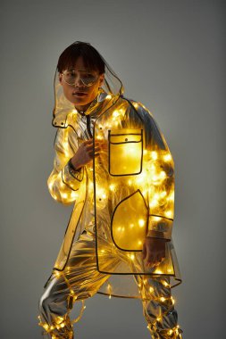 Genç bir Asyalı, sessiz bir arkaplanda parlayan ışıklarla modern bir kıyafeti büyülüyor..