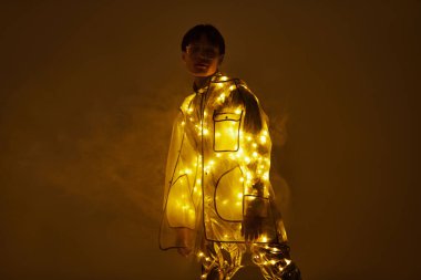 Yakışıklı Asyalı genç bir adam kendine güvenerek ayakta duruyor, ışıldayan parlak bir kıyafet içinde..