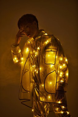 Genç, yakışıklı Asyalı bir adam zarif bir şekilde göz kamaştırıcı, ışıl ışıl bir kıyafetin içinde duruyor..