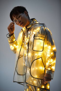 Şık, genç Asyalı bir adam, kendine güvenen bir şekilde parlak bir yağmurlukla poz veriyor, benzersiz tarzını sergiliyor..