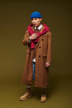 Şık kahverengi bir ceket ve mavi bir bere giyen Asyalı genç bir adam moda anlayışını sergiliyor..