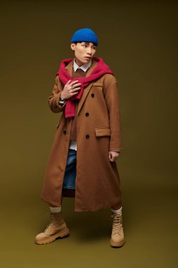 Tarz sahibi genç Asyalı adam, sıcak bir arka planda çarpıcı bir kıyafet giyerek kendine güvenerek ayakta duruyor..