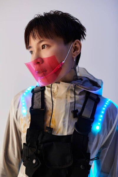 A young handsome Asian man is showcasing a futuristic outfit adorned with vibrant lights.