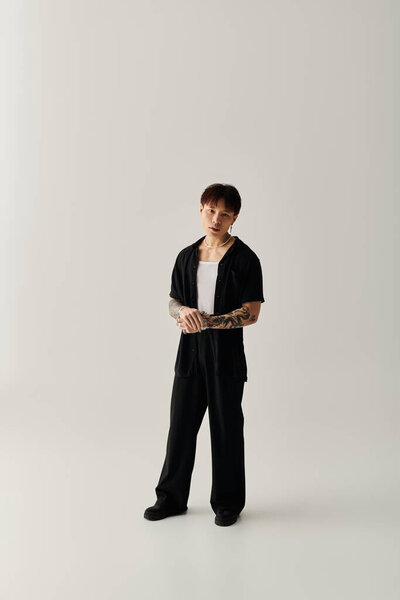 Молодой красивый азиат уверенно стоит в шикарном черном наряде на простом фоне.