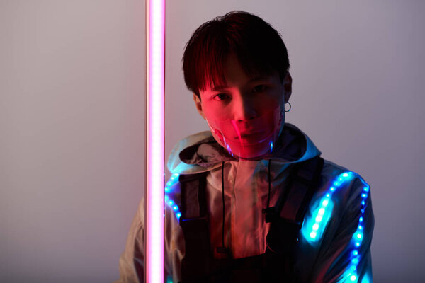 Стильный молодой азиат в футуристическом наряде светится под неоновыми огнями.