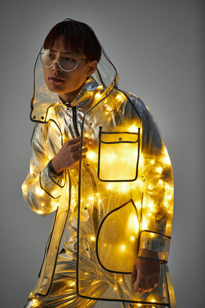 Молодой красивый азиат демонстрирует свой неповторимый стиль в светящемся плаще, выражая уверенность.