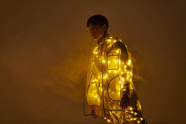 Молодой красивый азиатский мужчина уверенно позирует в светящемся наряде посреди золотой дымки.