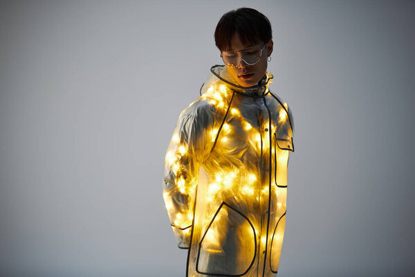 Молодой красивый азиат уверенно стоит в светящейся куртке в минималистской студии..