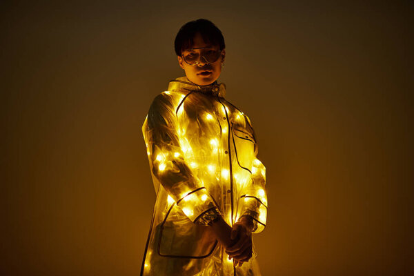 Молодой, красивый азиат уверенно стоит, украшенный светящимся нарядом, излучающим современный колорит.