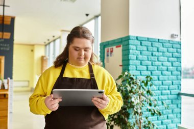 Down sendromlu genç bir kadın canlı bir kafe atmosferinde tablet kullanıyor..