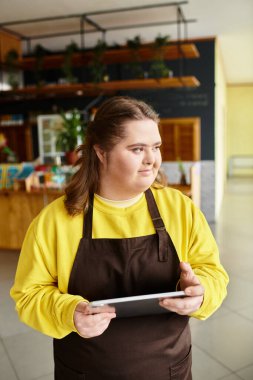 Dost canlısı bir kafede Down sendromlu genç bir kadın elinde tabletle müşterilerle bağlantı kuruyor..